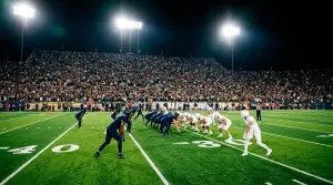 NFL night game under stadium floodlights with players lined up at scrimmage